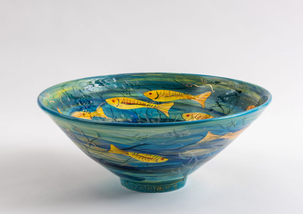 Large open bowl hand painted blue with yellow fish swimming around it.