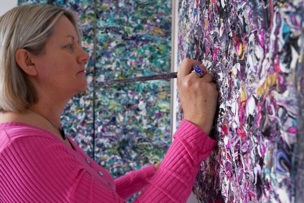 Artist Cherrie Mansfield in her studio looking at a large orange and white abstract painting