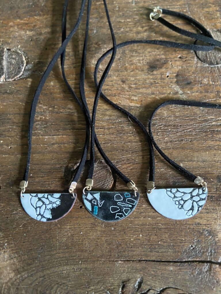 three necklaces with felt neck chains and half moon copper pendants decorated with pebble patterns in black, white & blue scraffito enamel